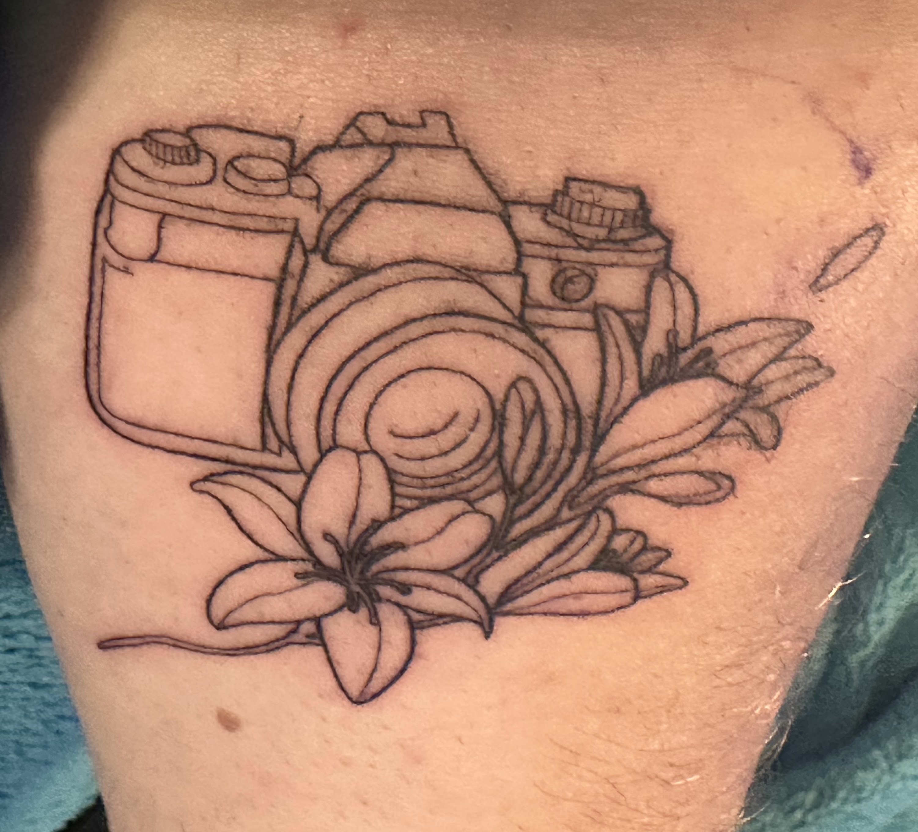 Foto van een fine line tatoeage van een vintage fototoestel en lelies. 